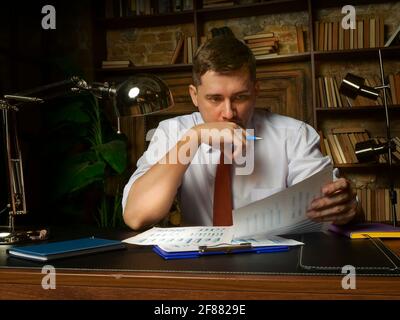 L'uomo d'affari stanco sta lavorando tardi con i documenti finanziari. Documenti e lavori di proprietà. Foto Stock