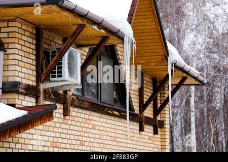 Grandi icicles appendono sotto il tetto di una casa privata. Caduta della molla. Foto Stock