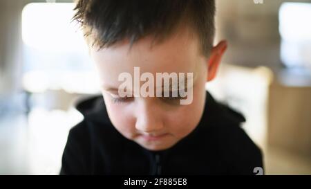 Povero ragazzo triste con sopracciglia tagliata in piedi in casa, concetto di povertà. Foto Stock