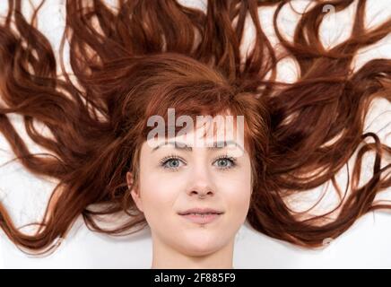 Ritratto di donna sorridente con capelli rossi davanti a sfondo bianco con lunghi capelli ricci intorno alla testa Foto Stock