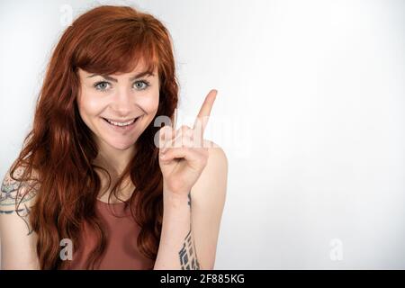 Ritratto di donna con capelli rossi davanti a sfondo bianco chi sta ponting in su mentre sorride Foto Stock