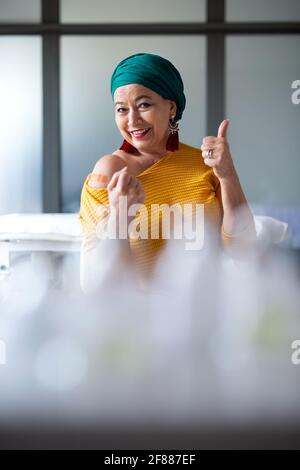 Donna anziana felice con sciarpa dopo la vaccinazione in ospedale, guardando la macchina fotografica. Foto Stock