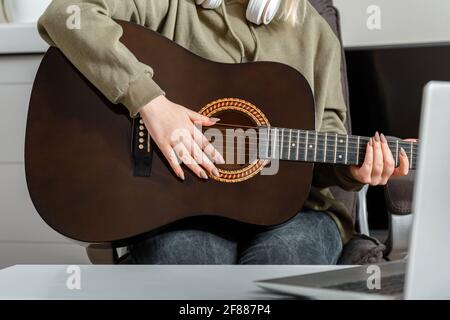 Corsi di formazione online per chitarra musica e formazione durante il blocco. Performance di chitarra musicale online. Giovane donna suona la chitarra acustica a casa Foto Stock