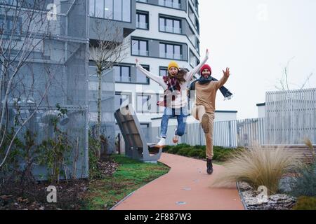 Allegro giovane coppia proprietari che saltano all'aperto di fronte a nuovo appartamento, nuovo concetto di casa e di rilocazione. Foto Stock