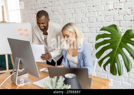 Gioiosi dipendenti multietnici che lavorano insieme in un ufficio moderno, sorridendo, facendo documenti. Colleghi di buon successo che discutono di un nuovo progetto o. Foto Stock