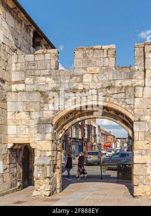 Una vista lungo una trafficata strada della città attraverso un antico arco tagliato in un muro. Le persone camminano lungo la strada e le auto guidano attraverso l'incrocio. Foto Stock