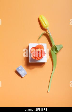 wabi sabi , concetto di design organico. Fiori in stile scandinavo e giapponese. Rosa arancio su marmo, tulipano giallo, minerale di cristallo su sfondo arancione Foto Stock