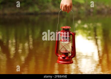 Lampada kerosene in mano sullo sfondo del fiume Foto Stock