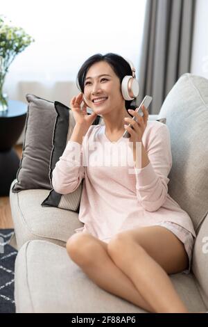 Felice giovane donna che indossa le cuffie sul divano Foto Stock