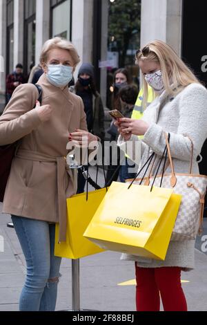 Londra, Inghilterra, 12 aprile 2021. Due donne con borse per la spesa fuori Selfridges in Oxford Street, come le restrizioni Covid sono attenuate consentendo negozi non essenziali di aprire. Fotografo : Brian Duffy Foto Stock