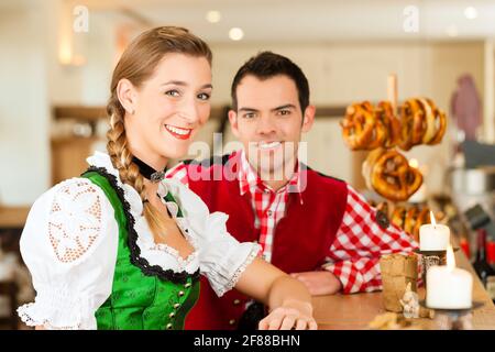Coppia giovane in tradizionali bavaresi Tracht nel ristorante o pub con pretzel Foto Stock