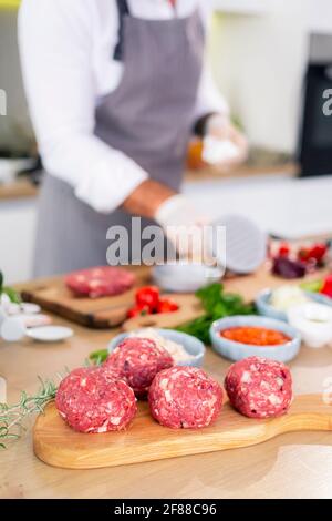 Chef che prepara polpette e le mette su una tavola di legno. Ci sono varie spezie, verdure, così come piccole bocce da cucina intorno al lavoro surf Foto Stock