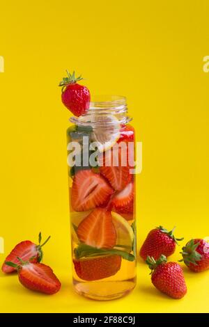 Infuso o detox acqua con fragola e limone in bottiglia sullo sfondo giallo.Copy space.Closeup. Foto Stock