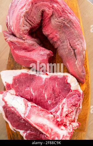 Pezzi di carne e di accompagnamento spezie e verdure fotografate su una tavola di legno sulla superficie di lavoro della cucina. Foto Stock