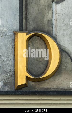 Lettera storica d'oro p con serifs su una parete grigia Foto Stock