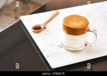 Caffè Dalgona, caffè frullato e cremoso in un bicchiere trasparente su sfondo di marmo accanto a un cucchiaio di legno. Molto popolare in Corea. Foto Stock