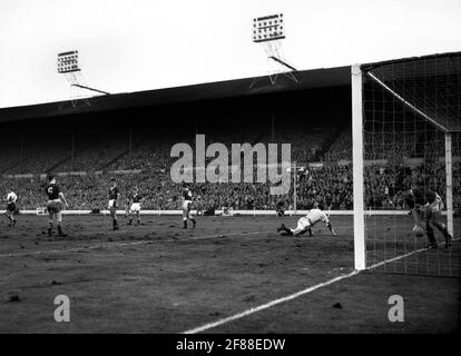 File photo datato 23-11-1960 di Graham Williams (Galles) raccogliendo la palla dalla rete dopo che Johnny Haynes ha segnato il quarto gol dell'Inghilterra. Altri giocatori gallesi visti L-R sono: Colin Baker (n° 6), Mel Nurse, Alan Harrington, Vic Crowe (n° 4) e il portiere Jack Kelsey. L'Inghilterra ha vinto la partita 5-1. Data di emissione: Lunedì 12 aprile 2021. Foto Stock