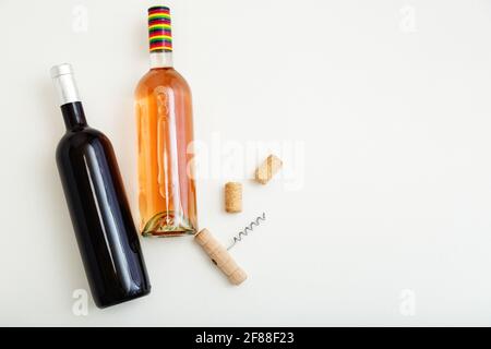 Bottiglia di vino rosato e bottiglia di vino rosso cavatappi e sughero. Composizione del vino minimalista vista dall'alto su sfondo bianco. Due bottiglie di vino marca mockup. Foto Stock