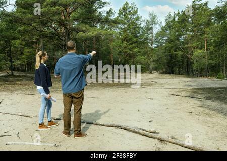 uomo e donna cercano un appezzamento di terra per costruzione di casa di campagna. copia spazio Foto Stock