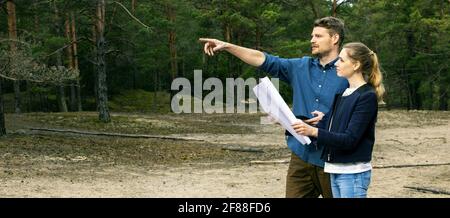 giovane coppia che sceglie un appezzamento di terra per costruzione di lodge di foresta. spazio di copia di banner Foto Stock