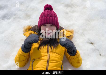 Ritratto di stile di vita di giovane felice e bella donna cinese asiatica giubbotto invernale giallo e cappello che gioca eccitato sdraiarsi sopra neve sensazione spensierata Foto Stock