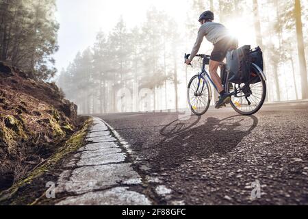 Ciclista in bicicletta con panniere che cavalcano lungo una nebbia strada forestale Foto Stock