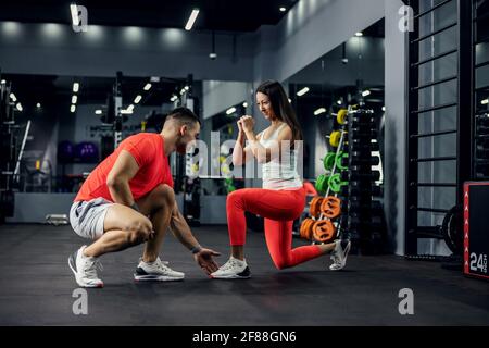 Un istruttore sportivo forma una persona sorridente motivata in palestra con attrezzature per l'allenamento. È in una posizione di passo con la guardia di boxe A. Foto Stock