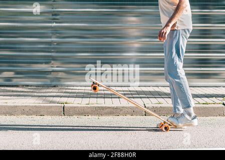 gambe di un uomo caucasico irriconoscibile che solleva uno skateboard con i piedi Foto Stock