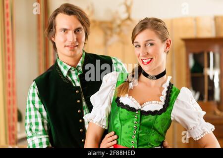 Coppia giovane in tradizionali bavaresi Tracht nel ristorante o pub, potrebbero essere i padroni di casa Foto Stock