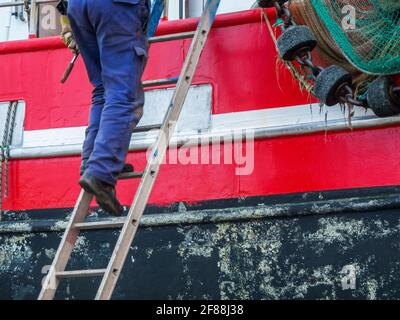 Vista parziale dello scafo di una nave in metallo nel bacino asciutto con una scala attaccata e lavoratori irriconoscibili su di essa. Foto Stock