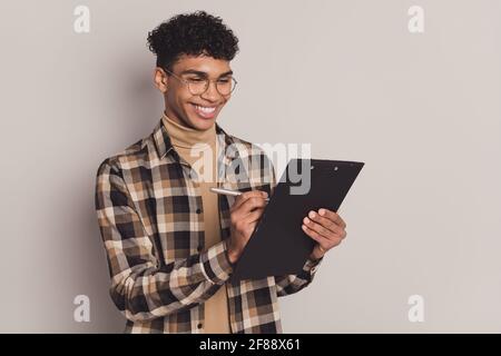 Ritratto fotografico dell'esame di prova di scrittura del ragazzo sull'intervista di clipboard sorridente isolato su sfondo grigio Foto Stock