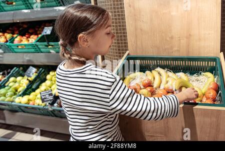 Una bambina sceglie le mele e le banane confezionate singolarmente nel negozio. Foto Stock