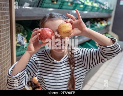 La bambina felice sceglie le mele in un negozio di alimentari. Shopping di alimentari divertente. Foto Stock