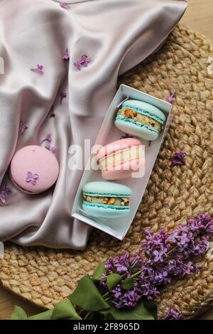 macaroni o macaroni francesi rosa e menta in scatola regalo e fiori lilla su un panno e paglia di sfondo. Frutta naturale e bacca Foto Stock