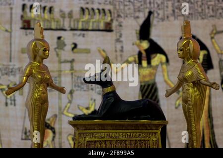 Ancora vita con figure egiziane di anubis e la dea nebtht ed eset in oro. Sullo sfondo sono antichi disegni egizi. Foto Stock