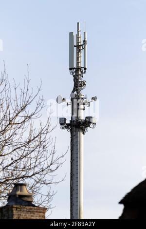 Un ritratto in primo piano di una parte superiore di un palo del telefono o di una torre di trasmissione in piedi alto nel cielo blu. L'antenna e le piastre satellitari sono visibili Foto Stock