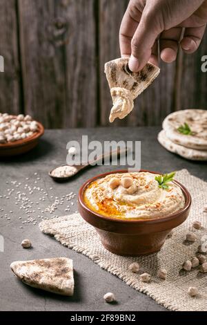 Immersione a mano del pane pita in hummus su sfondo scuro formato verticale. Foto Stock