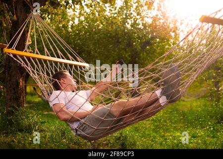 uomo prendere selfie in amaca in foresta in giorno di sole. concetto di riposo in foresta tropicale Foto Stock