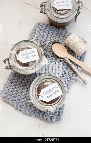 Tre vasetti ricoperti di mousse di cioccolato su un panno blu lavorato accanto con un paio di cucchiai al centro e tre etichette sui vasetti. Foto Stock