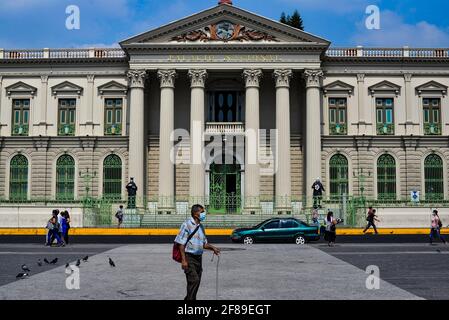 Un uomo che indossa un facemask come precauzione contro la diffusione di covid-19 passeggiate di fronte al Salvadoran National Palace.El Salvador riporta più di 66 mila casi confermati COVID-19 così come 2,054 morti. Foto Stock