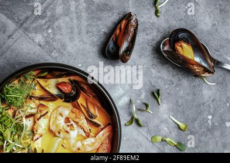 Thai Tom Yam zuppa piccante con frutti di mare, popolare cucina tailandese. Su sfondo grigio argilloso con cozze Foto Stock