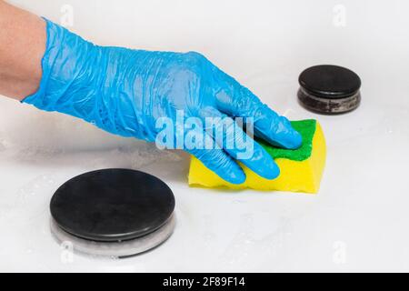La mano femminile di una casalinga in un guanto domestico di lattice lava la stufa a gas con una spugna, primo piano. Foto Stock