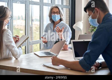 Persone che lavorano in squadra indossando maschere mediche durante la riunione in ufficio. Foto Stock