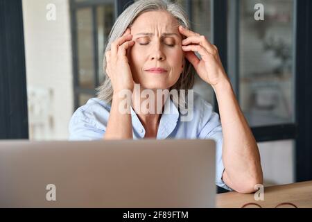 Stressato senior 60 anni massaggiante testa in ufficio a casa, soffrendo sul posto di lavoro. Foto Stock