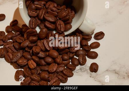 Alcuni chicchi di caffè ricchi che escono da una tazza distesa da un lato Foto Stock