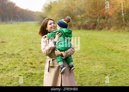 Donna che tiene un bambino tra le braccia. La famiglia si diverte nel parco autunnale. Madre e figlio. Foto Stock