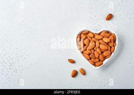 Dado a mandorla in una piastra di ceramica a forma di cuore su sfondo bianco con spazio per la copia. Snack vegan cibo senza zucchero. Foto Stock