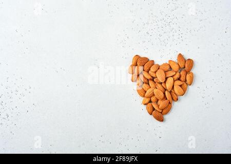 Mandorle di noce disposte a forma di cuore su sfondo bianco con spazio di copia. Concetto di cibo di dieta. Snack vegan cibo senza zucchero. Foto Stock