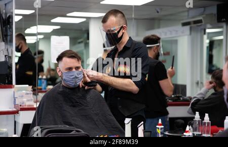 Londra, Regno Unito. 12 Aprile 2021. Un parrucchiere che indossa una maschera e uno scudo taglia i capelli di un cliente durante la riapertura. Negozi, ristoranti, bar e altre aziende hanno riaperto oggi dopo quasi quattro mesi, mentre le ulteriori regole di blocco sono rilassate in Inghilterra. (Foto di Yunus Dalgic/SOPA Images/Sipa USA) Credit: Sipa USA/Alamy Live News Foto Stock