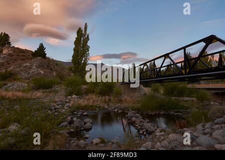 Panorama di un ponte ferroviario di ferro contro le montagne durante il tramonto a Esquel, Patagonia, Argentina Foto Stock